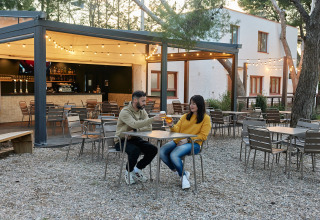 Koppel proost op terras met lichtjes bij TAIGA Lake Caspe vakantiepark in Aragón, Spanje.