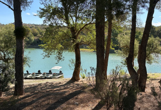 Blick durch Bäume auf den ruhigen See TAIGA Lake Caspe in Aragón, Spanien, mit Booten am Ufer.