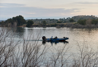 Un bateau à moteur navigue sur le lac au parc de vacances TAIGA Lake Caspe en Aragon, Espagne, sous un ciel paisible.