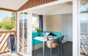 Lys, moderne Beach Lodge ved Arden Parks Tulderheyde i Belgien med terrasse og surfbræt udenfor.