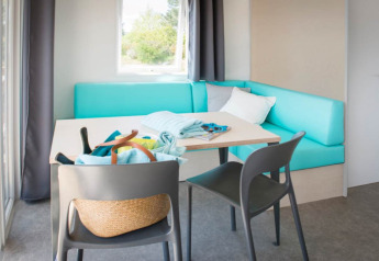 Area soggiorno luminosa e moderna con divano turchese, tavolo e sedie alle Beach Lodges, Arden Parks Tulderheyde.