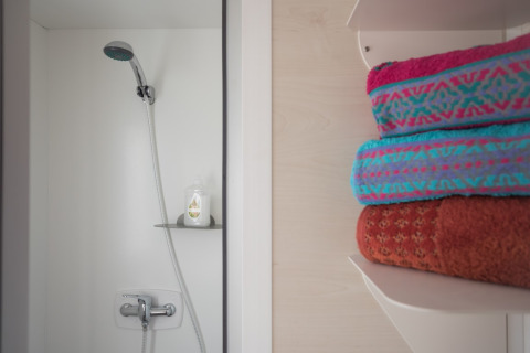 Doccia con soffione a mano e asciugamani colorati su mensola presso Beach Lodges, Arden Parks Tulderheyde, Belgio.
