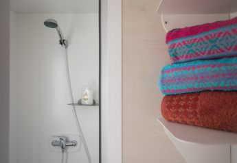 Doccia con soffione a mano e asciugamani colorati su mensola presso Beach Lodges, Arden Parks Tulderheyde, Belgio.