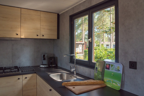 Moderne lodge keuken met lichte kasten, uitzicht op het groen en een stokbrood op het aanrecht.