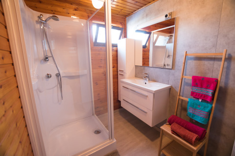 Moderne badkamer met douche, houten muren en kleurrijke handdoeken bij Luxe Lodges in Tulderheyde, België.