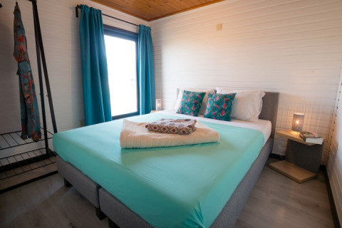 Moderne slaapkamer met dubbel bed, turquoise gordijnen en kussens in Luxe Lodges, Arden Parks Tulderheyde, België.