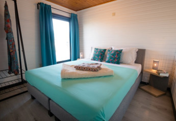 Camera moderna con letto matrimoniale, tende turchesi e cuscini presso Luxe Lodges, Arden Parks Tulderheyde, Belgio.