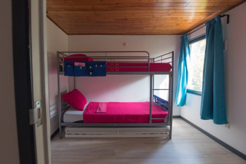 Et moderne værelse med køjeseng, røde dyner og blå gardiner på Luxe Lodges, Arden Parks Tulderheyde, Belgien.