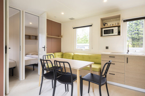 Interno luminoso di Cordelia Lodges ad Arden Parks Tulderheyde, Belgio, con cucina, tavolo e camere da letto.