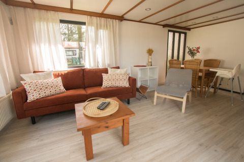 Woonkamer van Sun Lodge in Arden Parks Tulderheyde, België, met zetel, stoel, eettafel en veel daglicht.