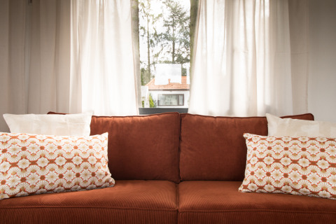 Knusse bruine sofa met sierkussens voor lichte gordijnen in Sun Lodge, Arden Parks Tulderheyde, België.
