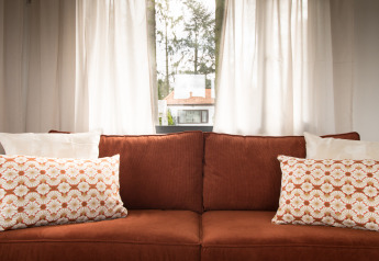 Knusse bruine sofa met sierkussens voor lichte gordijnen in Sun Lodge, Arden Parks Tulderheyde, België.
