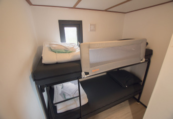 Stapelbedkamer met raam in Sun Lodge op Arden Parks Tulderheyde in België, donker beddengoed aanwezig.