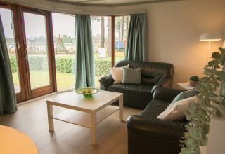 Woonkamer met lederen zetels, salontafel en grote ramen in Sun Lodge, Arden Parks Tulderheyde, België.