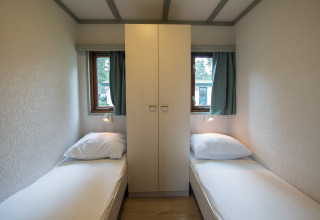 Kleine kamer met twee enkele bedden, een kast in het midden en twee ramen in Sun Lodge, Arden Parks Tulderheyde.