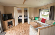 Stue i Sun Lodge Comfort ved Arden Parks Tulderheyde, Belgien, med hjørnesofa, tv og pejseovn.