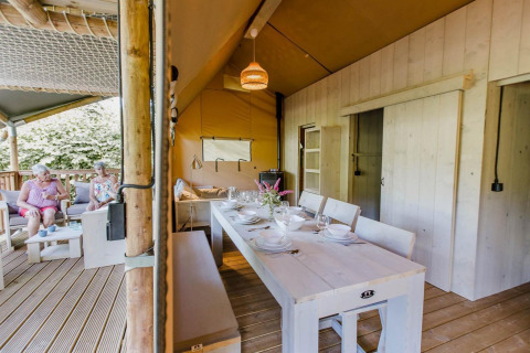 Udendørs spiseområde og opholdsstue i Ranger Lodge ved Arden Parks Tulderheyde, Belgien, med to kvinder.