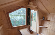 Acogedora cabaña de glamping con interior de madera clara, gran ventana y vistas a la naturaleza exterior.