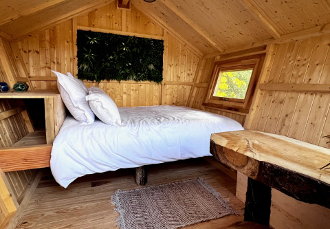 Gezellige houten glampinghut met tweepersoonsbed, witte lakens en rustiek houtwerk in een bosrijke omgeving.