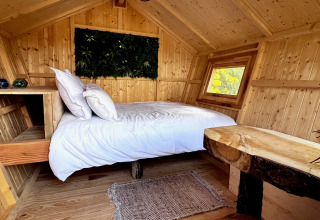 Gezellige houten glampinghut met tweepersoonsbed, witte lakens en rustiek houtwerk in een bosrijke omgeving.