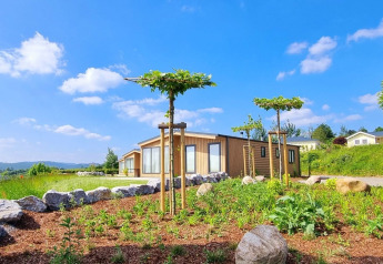 Chalet Enzian features modern wood exteriors, young trees, rocks, and gardens under a bright blue sky.
