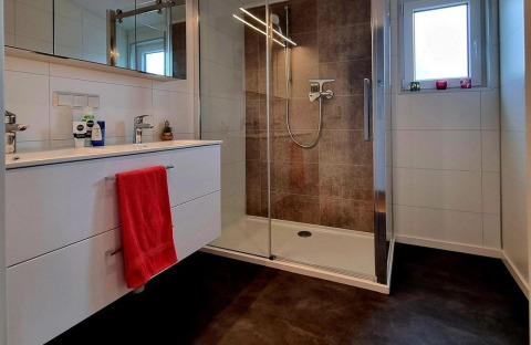 Baño moderno con ducha acristalada, doble lavabo y toalla roja en Chalet Enzian, Brilon, Alemania.