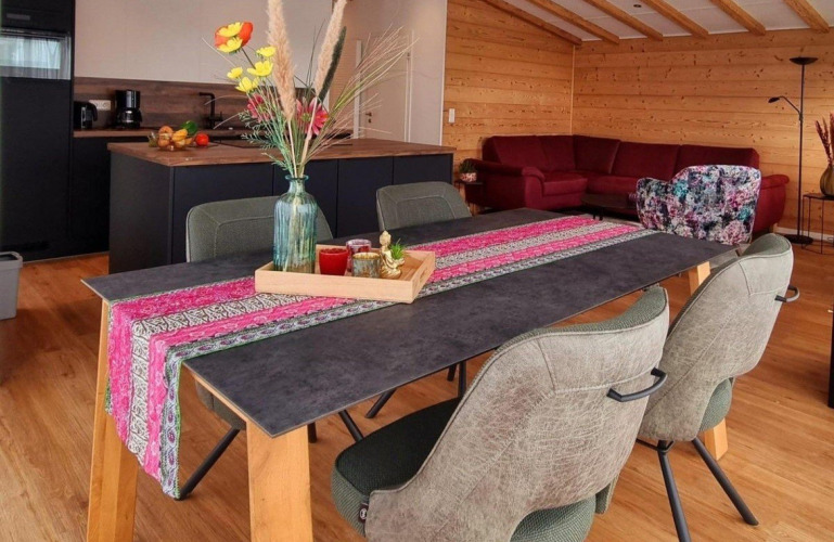 Mesa de comedor con camino de colores y jarrón en cabaña moderna de madera, Chalet Enzian, Camping & Ferienpark Brilon, Alemania.