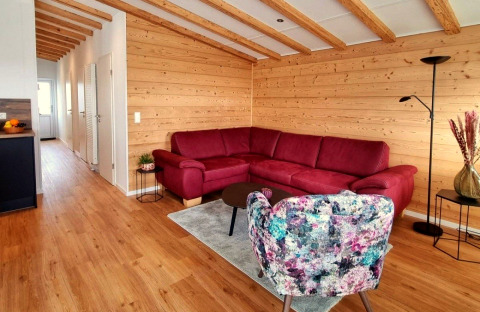 Living room in Chalet Enzian at Camping & Ferienpark Brilon with red sofa, wood walls and beams.