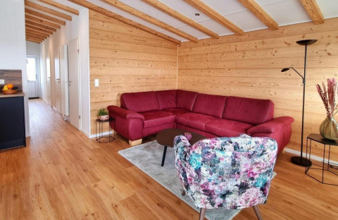 Living room in Chalet Enzian at Camping & Ferienpark Brilon with red sofa, wood walls and beams.