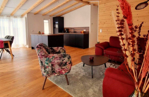 Cozy living area with wood beams, modern kitchen, and colorful chairs at Chalet Enzian, Camping & Ferienpark Brilon.
