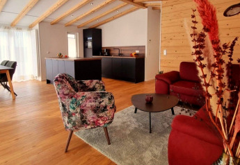 Gezellige woonkamer met houten balken, moderne keuken en kleurrijke stoelen in Chalet Enzian, Brilon.