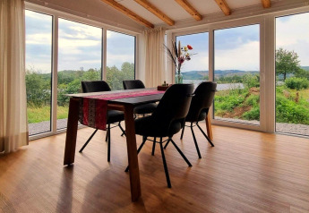 Eetruimte in Chalet Enzian, Camping & Ferienpark Brilon, met uitzicht op groene heuvels door grote ramen.