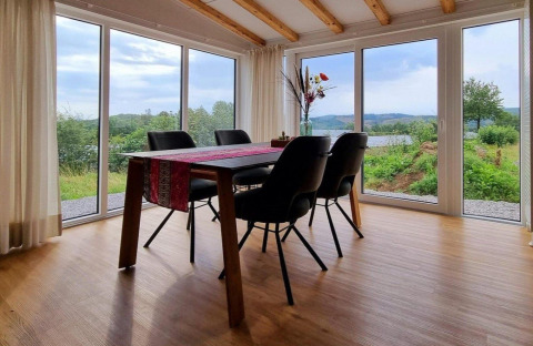 Eetruimte in Chalet Enzian, Camping & Ferienpark Brilon, met uitzicht op groene heuvels door grote ramen.