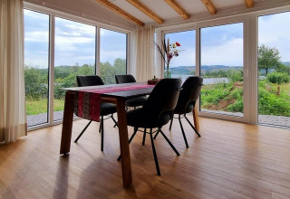 Eetruimte in Chalet Enzian, Camping & Ferienpark Brilon, met uitzicht op groene heuvels door grote ramen.