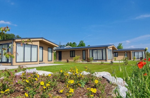 Chalet Enzian bij Camping & Ferienpark Brilon in Duitsland, moderne huisjes met bloemen en helderblauwe lucht.