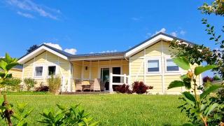 Bright yellow mobile home, Chalet Limonet, with a covered porch, set in a green garden under blue sky.