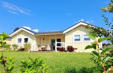 Mobil-home jaune Chalet Limonet, terrasse couverte et jardin vert sous un ciel bleu éclatant.