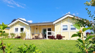 Gelbes Mobilheim Chalet Limonet mit überdachter Terrasse, umgeben von grünem Rasen bei Sonnenschein.