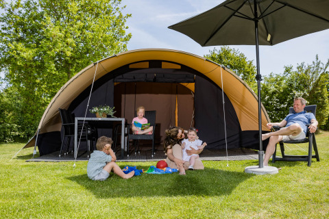 Gezin voor een De Waard tunneltent met privé sanitair, kinderen spelen op het gras onder de zon.