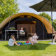 Gezin voor een De Waard tunneltent met privé sanitair, kinderen spelen op het gras onder de zon.