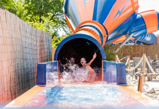 Twee kinderen glijden lachend uit een waterglijbaan in Kampeerdorp de Zandstuve, Nederland.