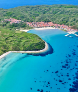 Luchtfoto van Mali Lošinj, Kroatië met turquoise zee, groene heuvels en een kustplaats op de achtergrond.
