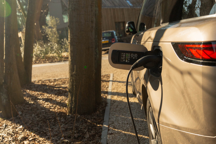 Coche eléctrico cargándose al aire libre en Suite at Woodz Lodges en Bélgica, rodeado de árboles.