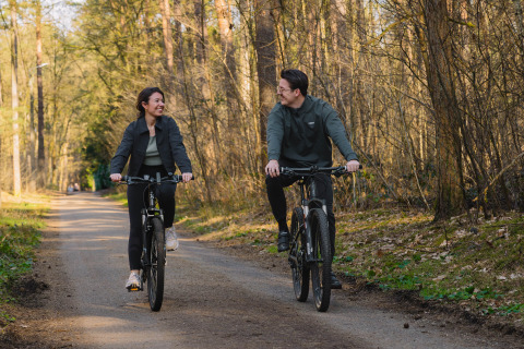 Twee mensen fietsen op een bospad bij Suite at Woodz Lodges in België, tussen de lentebomen.
