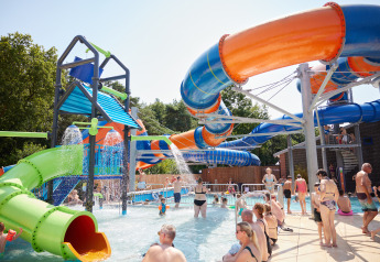 Famiglie si rilassano e giocano in un parco acquatico glamping con scivoli colorati in una giornata soleggiata.