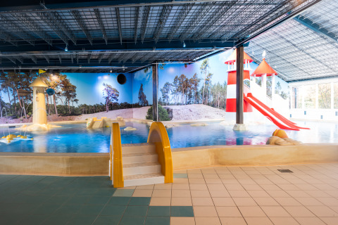 Piscina interna con scivoli colorati e area giochi per bambini in una struttura di glamping.