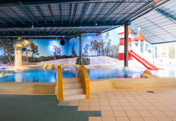 Overdekt zwembad met felgekleurde glijbanen en speelzone voor kinderen bij een glampingverblijf.