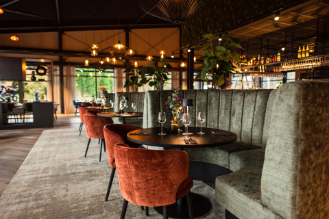 Restaurant chic dans un lieu de glamping avec fauteuils en velours, banquettes hautes et éclairage soigné.