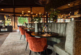 Restaurante moderno en glamping, con sillones de terciopelo, cabinas altas y luminarias elegantes.