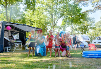 Bambini e adulti giocano con pistole ad acqua davanti a una tenda glamping in un campeggio estivo.